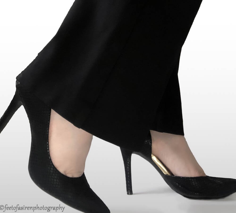 Structure for growth.  Black and gold heels on a white background being worn by a person in long black slacks.